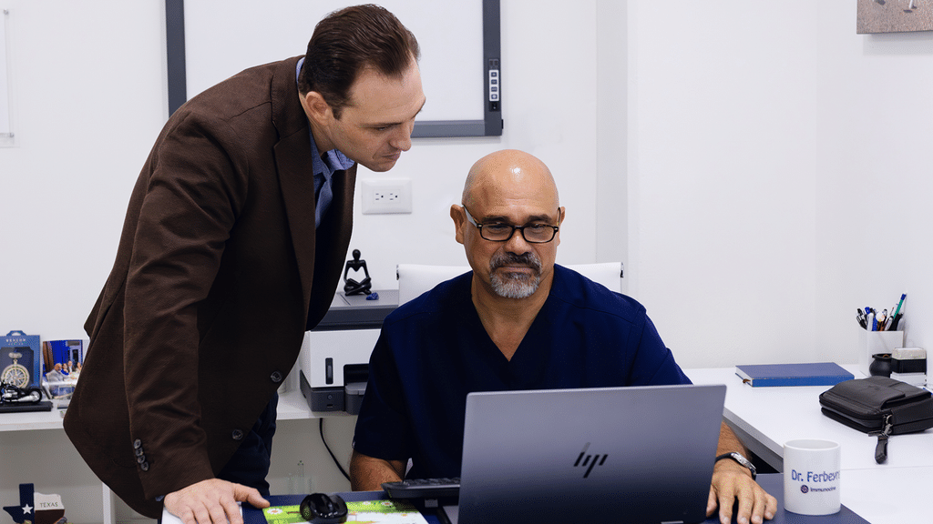 Two Immunocine team members reviewing work together on a laptop in an office.